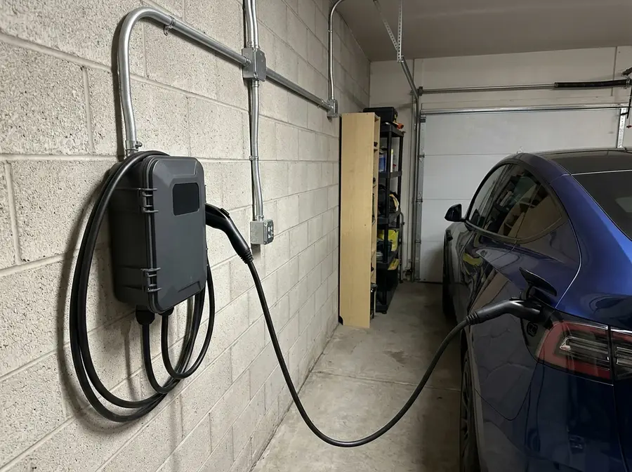 A wall-mounted EV charger hard-wired in a Parker garage with its cable plugged into a car, conduit from the charger joined into the wall run at both ends